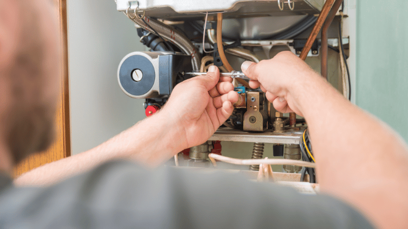 Technician adjusting internal furnace components during a residential heating system repair.