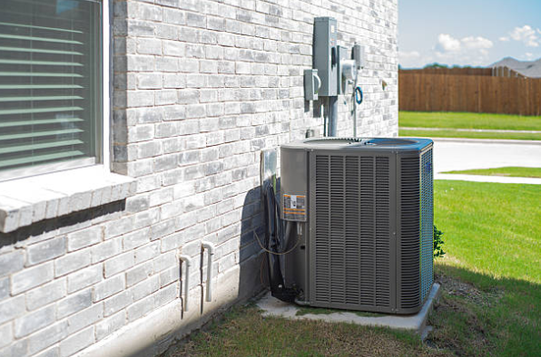An outdoor air conditioning condenser unit is installed on a concrete pad beside a brick home with electrical connections mounted above it.