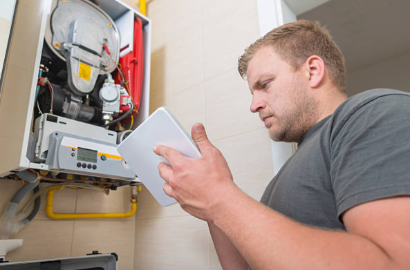 An HVAC technician uses a tablet to diagnose a wall mounted boiler system during a maintenance inspection.